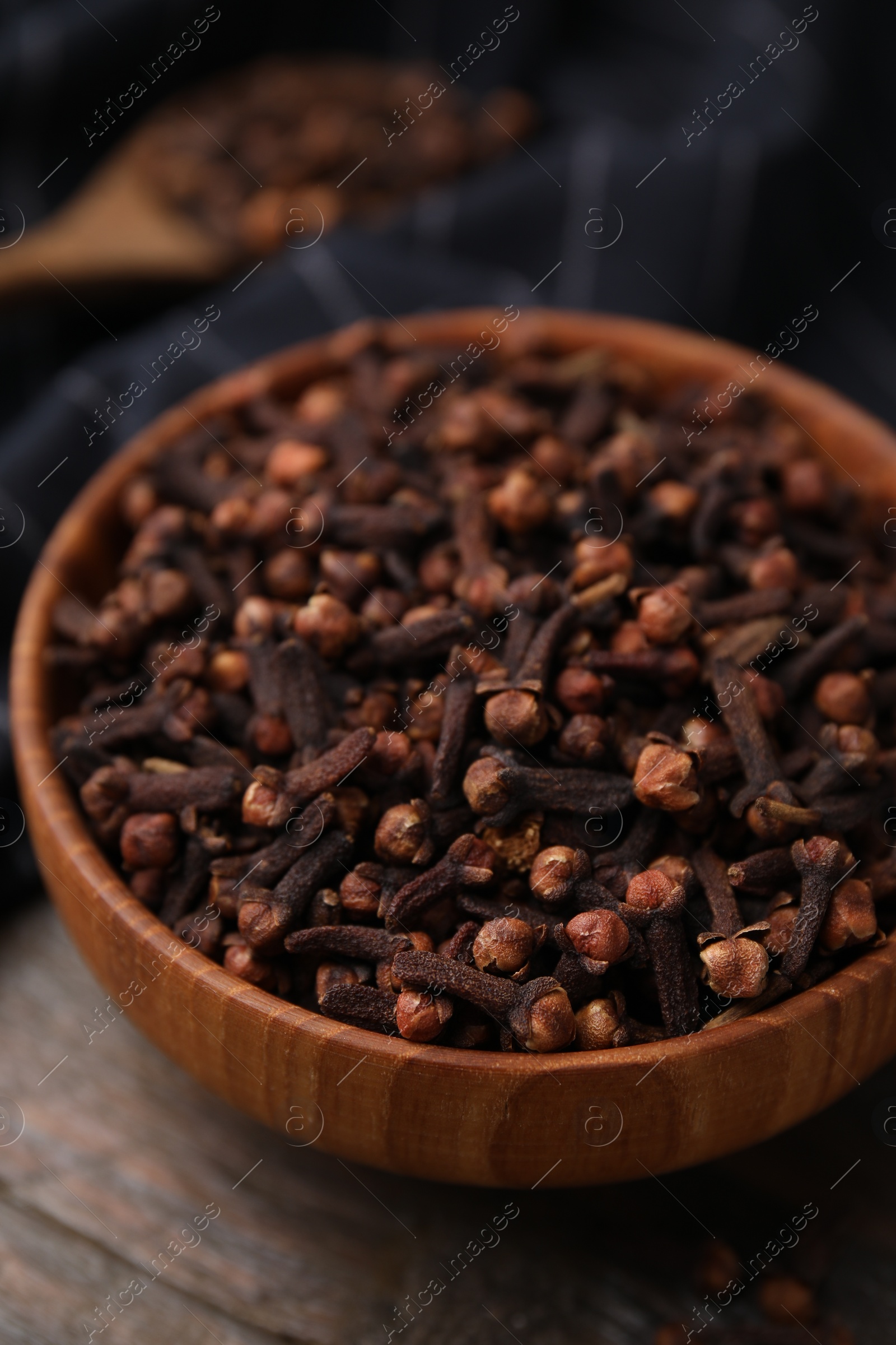 Photo of Aromatic cloves in bowl on wooden table, closeup