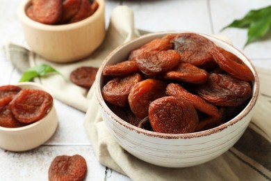 Photo of Tasty apricots in bowls on white tiled table, closeup. Dried fruits