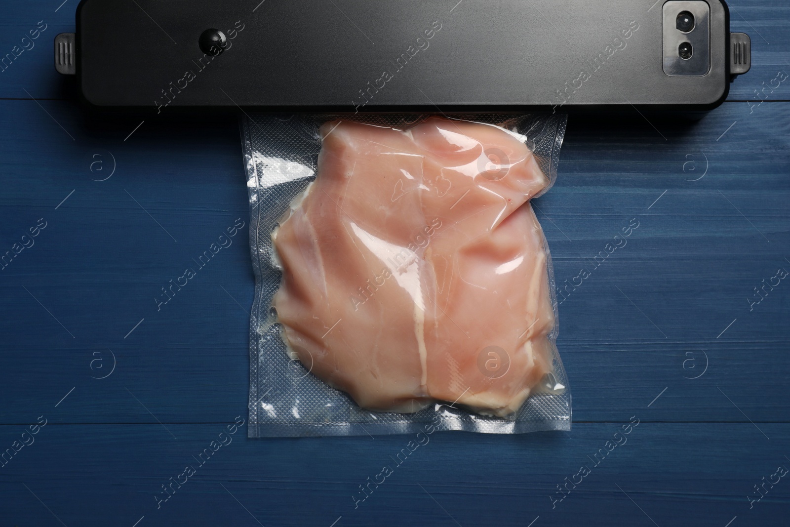 Photo of Sealer for vacuum packing and plastic bag with meat on blue wooden table, top view