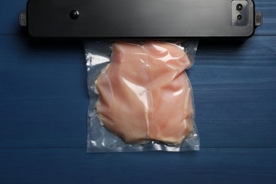 Photo of Sealer for vacuum packing and plastic bag with meat on blue wooden table, top view
