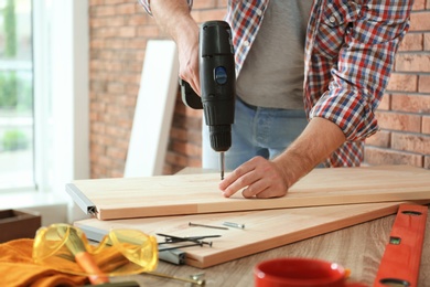 Photo of Young man working with electric screwdriver near brick wall
