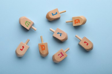 Photo of Wooden dreidels on light blue background, flat lay. Traditional Hanukkah game