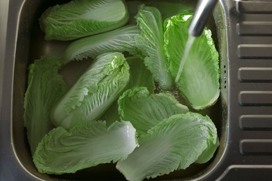 Photo of Pouring tap water on Chinese cabbage leaves in sink, top view