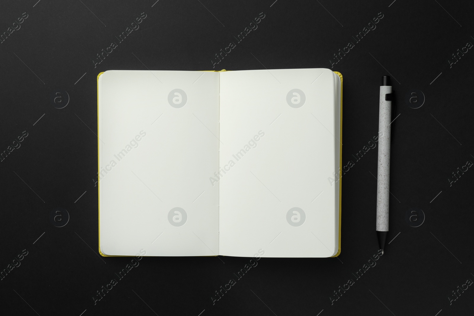 Photo of Open notebook with blank pages and pen on black background, top view. Space for text
