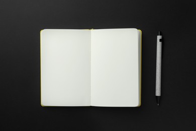 Open notebook with blank pages and pen on black background, top view. Space for text
