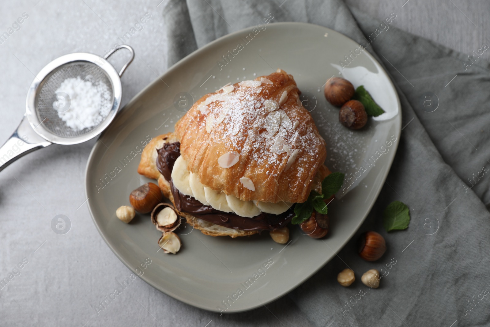 Photo of Delicious croissant with banana, chocolate and hazelnuts on gray table, flat lay