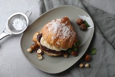 Delicious croissant with banana, chocolate and hazelnuts on gray table, flat lay