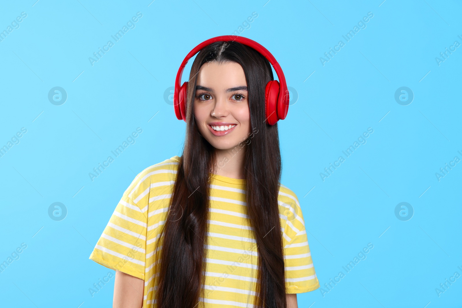 Photo of Teenage girl listening music with headphones on light blue background