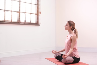 Photo of Young woman meditating in empty room, space for text. Zen concept
