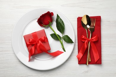 Beautiful place setting with dishware, gift and rose for romantic dinner on white wooden table, flat lay
