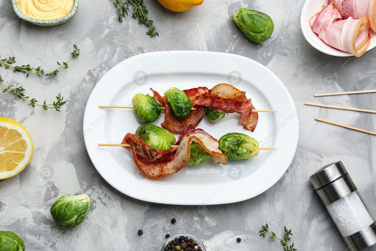 Photo of Skewers with Brussels sprouts and bacon in plate on grey table, flat lay