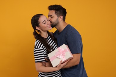 Man kissing his smiling girlfriend on orange background. Celebrating holiday