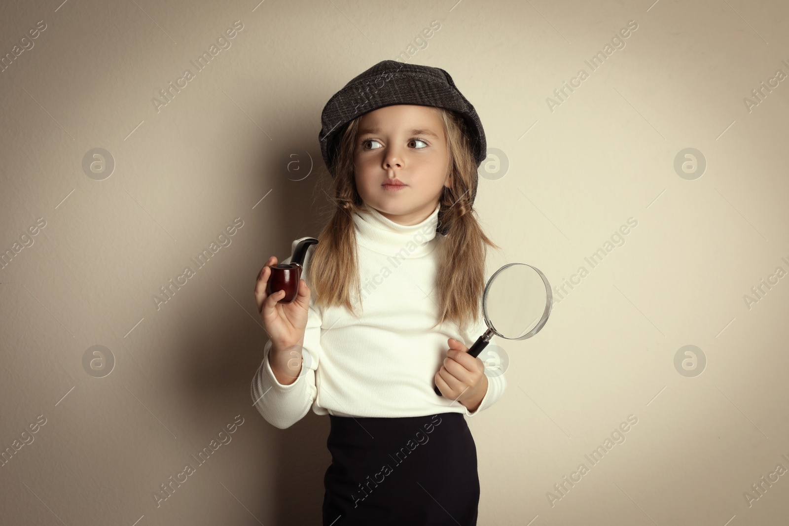 Photo of Cute little child in hat with smoking pipe and magnifying glass playing detective on beige background