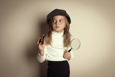 Photo of Cute little child in hat with smoking pipe and magnifying glass playing detective on beige background