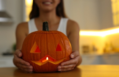 Photo of Woman holding pumpkin jack o'lantern at wooden table indoors, closeup with space for text. Halloween celebration