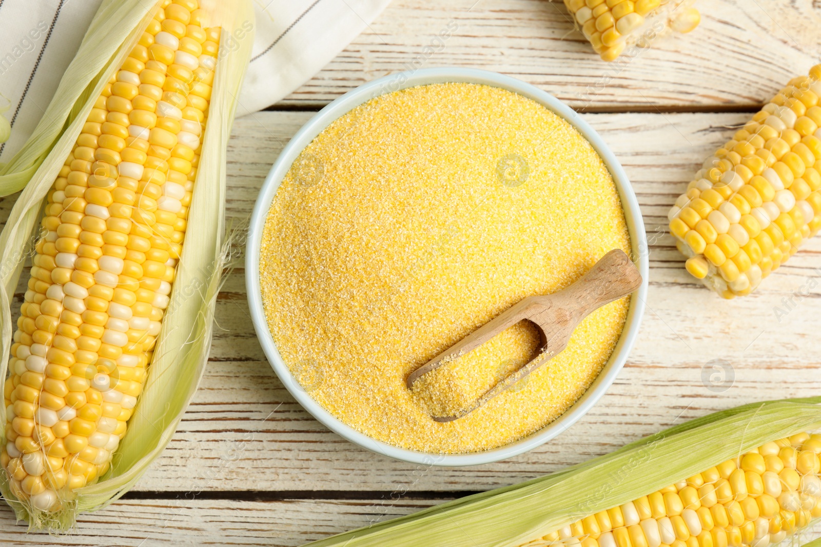 Photo of Cornmeal in bowl and fresh cobs on white wooden table, flat lay