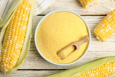 Cornmeal in bowl and fresh cobs on white wooden table, flat lay