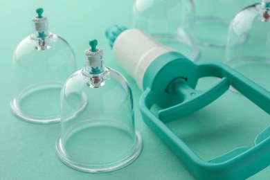 Photo of Plastic cups and hand pump on turquoise background, closeup. Cupping therapy