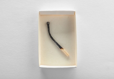Photo of Cardboard box with burnt match on white background, top view