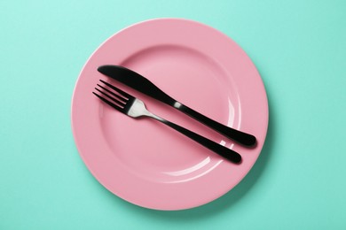 Pink ceramic plate and cutlery on turquoise background, top view