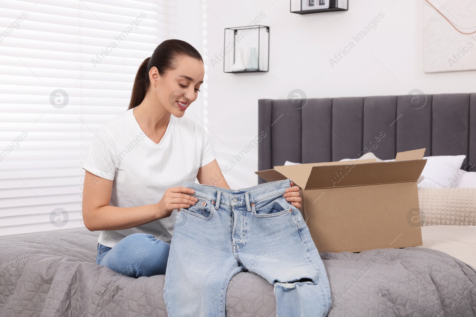 Photo of Happy woman with stylish light blue jeans at home. Online shopping