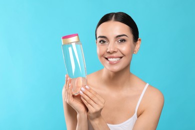 Photo of Young woman with bottle of micellar water on light blue background