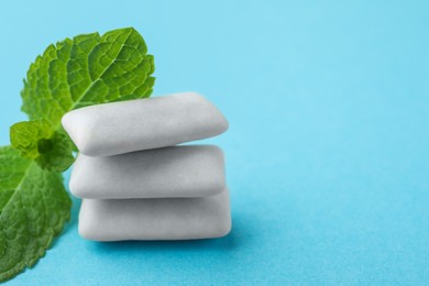 Photo of Tasty white chewing gums and mint leaves on light blue background, closeup. Space for text