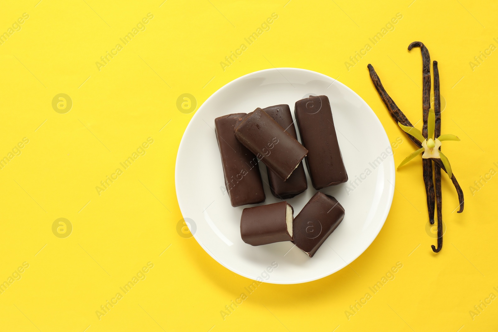 Photo of Glazed curd cheese bars, vanilla pods and flower on yellow background, top view. Space for text