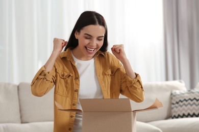 Photo of Emotional young woman opening parcel at home. Internet shopping