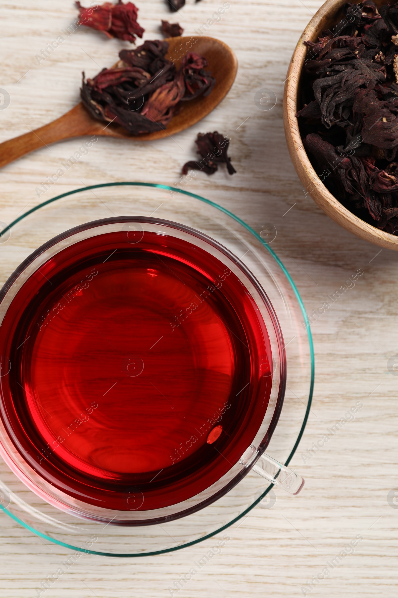 Photo of Cup of fresh hibiscus tea and dry flower leaves on wooden table, flat lay