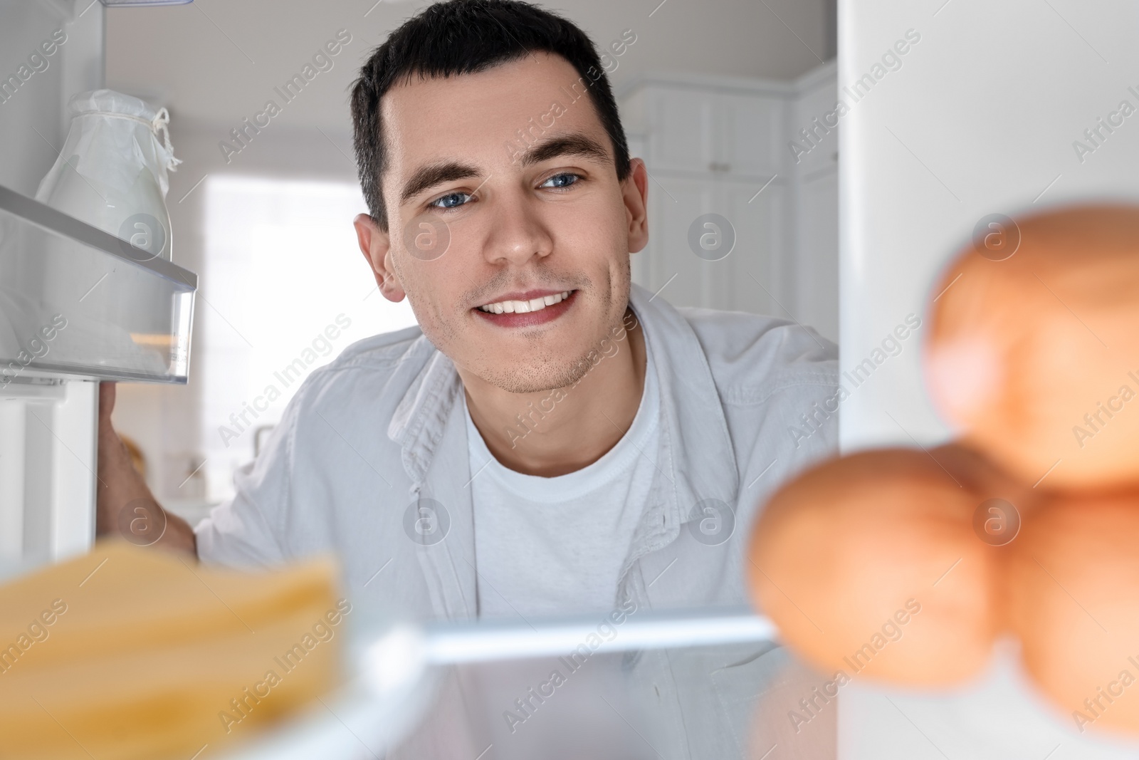 Photo of Happy man near refrigerator in kitchen, view from inside