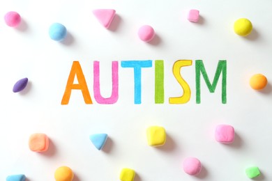 Photo of Word Autism and colorful plasticine figures on white background, flat lay