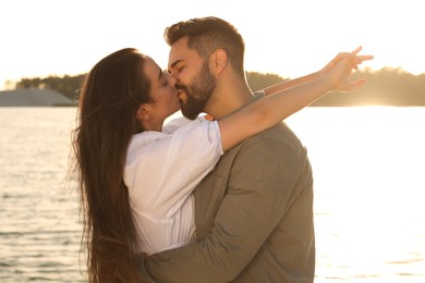 Happy couple kissing near river on sunny day