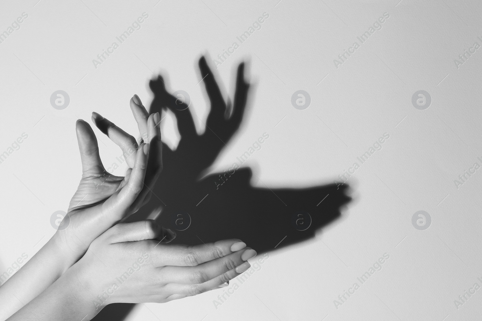 Photo of Shadow puppet. Woman making hand gesture like deer on light background, closeup with space for text. Black and white effect