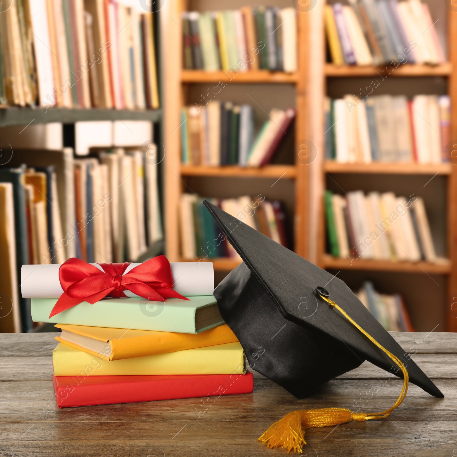 Image of Graduation hat, books and diploma on wooden table in library