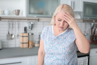 Mature woman suffering from headache in kitchen