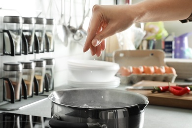 Photo of Woman salting boiling water in pot on stove, closeup