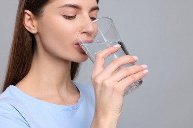 Photo of Healthy habit. Woman drinking fresh water from glass on grey background