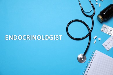 Endocrinologist. Stethoscope, pills and notebook on light blue background, flat lay