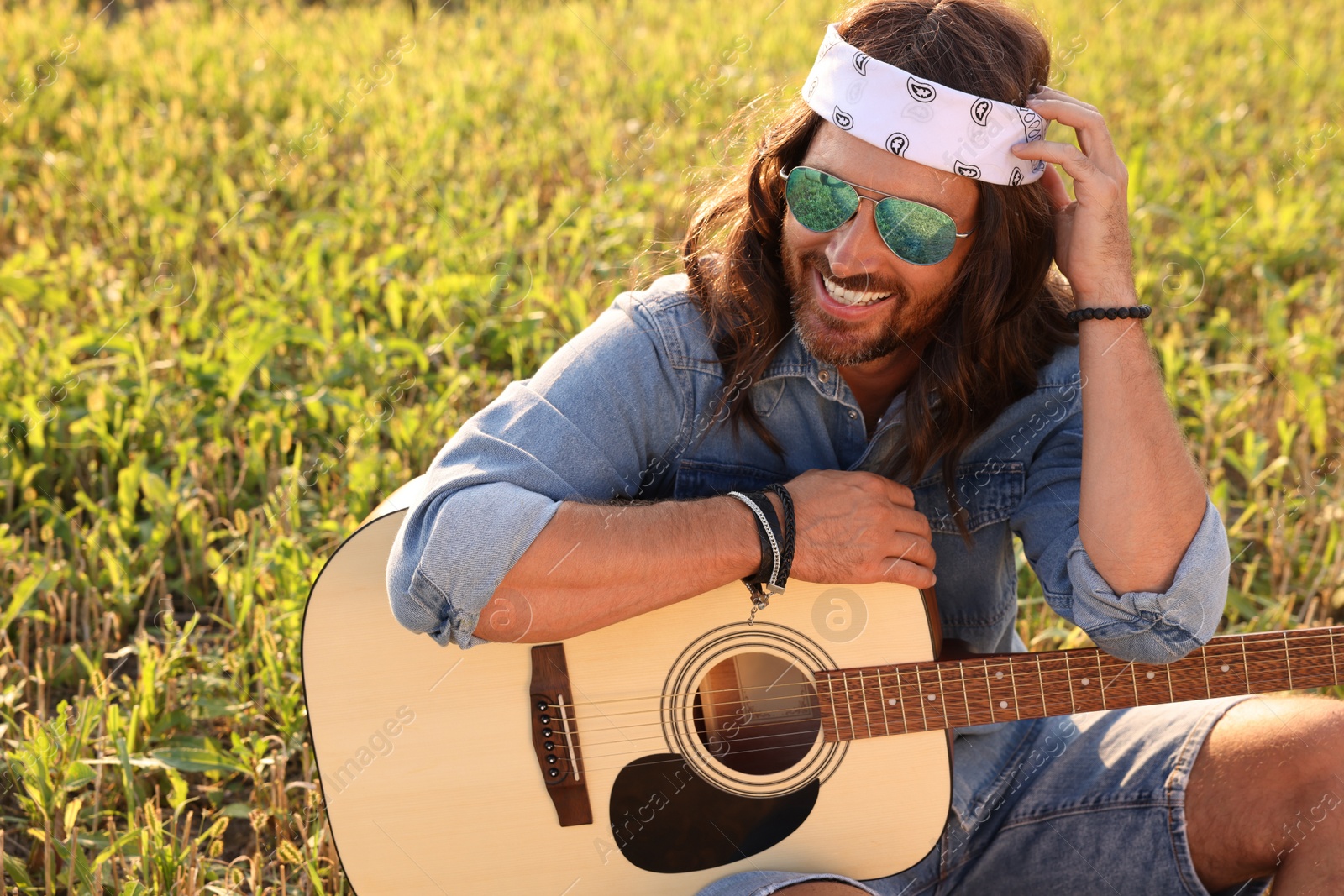 Photo of Portrait of happy hippie man with guitar in field