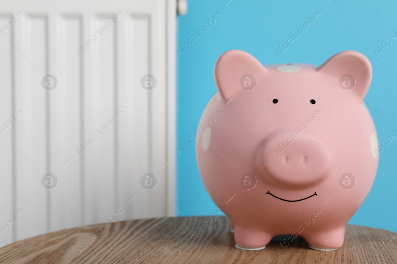 Photo of Piggy bank on wooden table near heating radiator, space for text