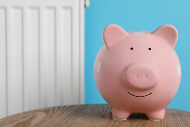 Photo of Piggy bank on wooden table near heating radiator, space for text