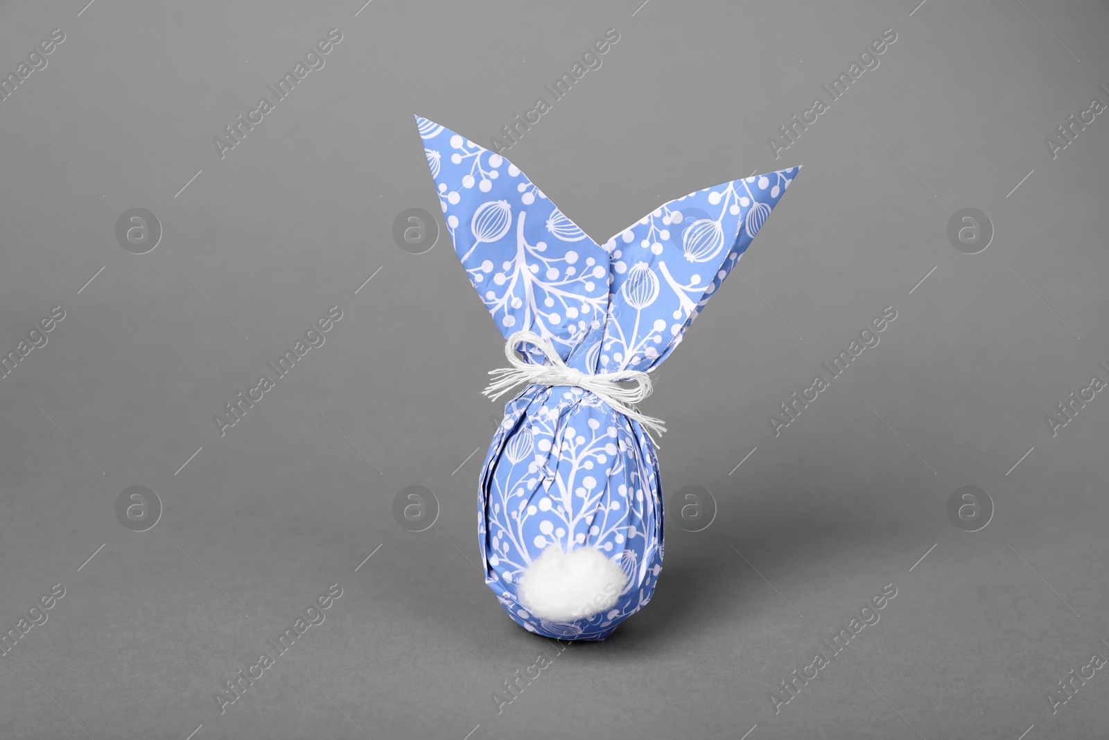 Photo of Easter bunny made of wrapping paper and egg on grey background