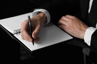 Photo of Man writing in notebook at black table, closeup