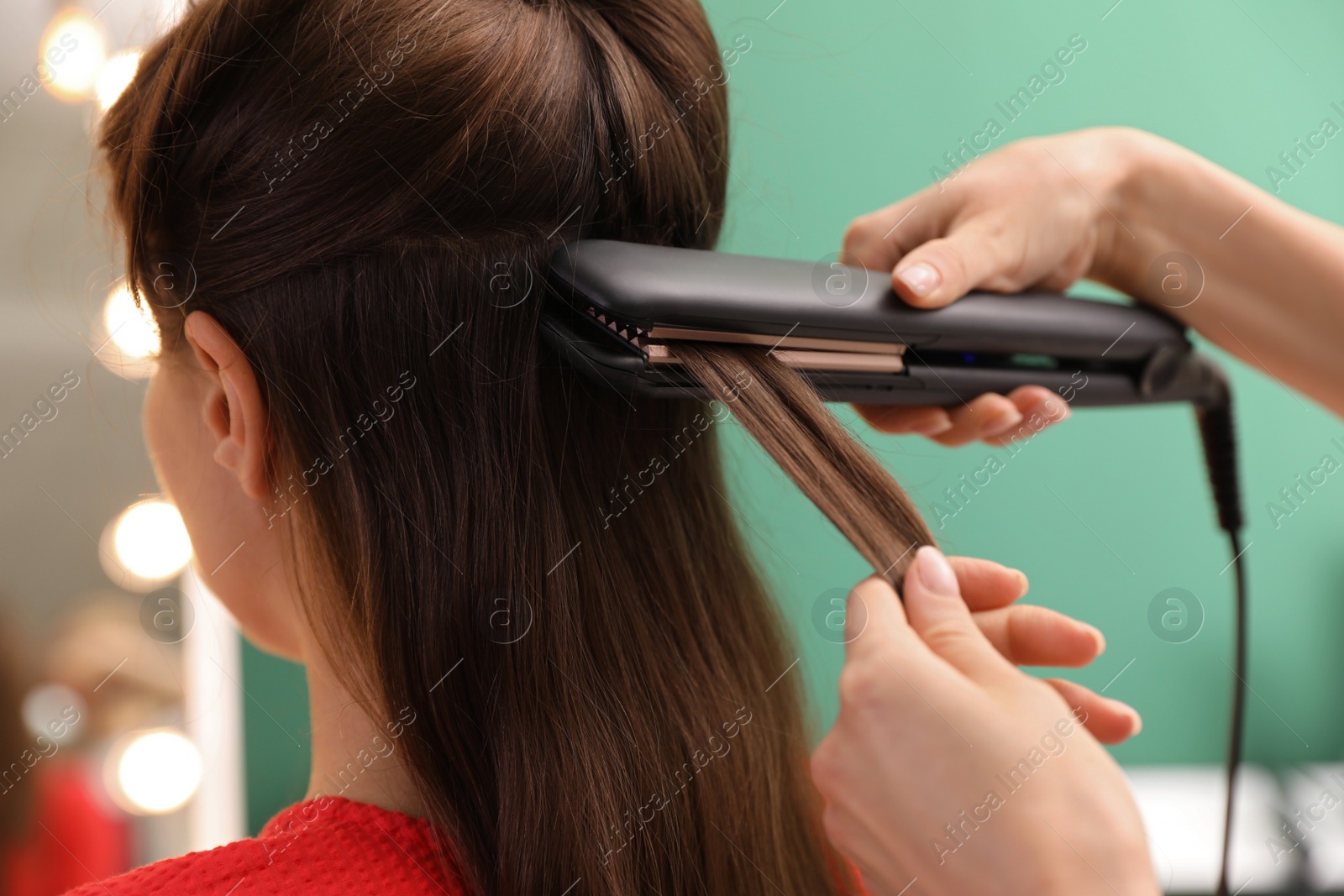 Photo of Stylist straightening woman's hair with flat iron in salon