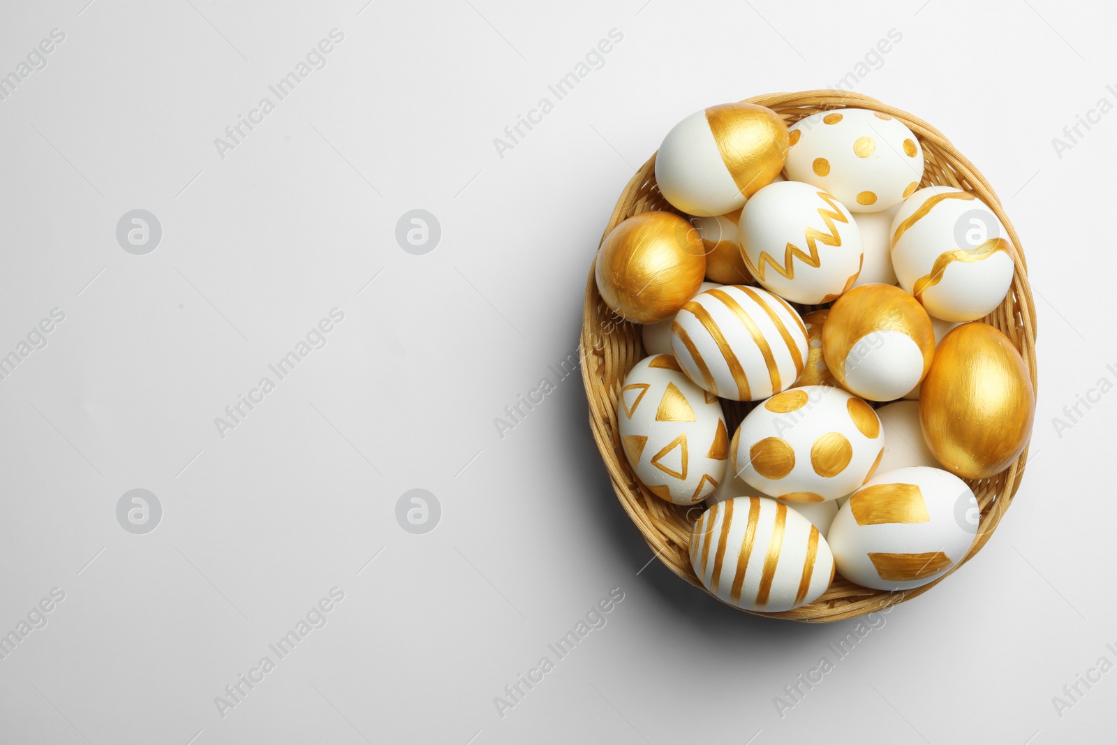 Photo of Wicker basket of traditional Easter eggs decorated with golden paint on white background, top view. Space for text