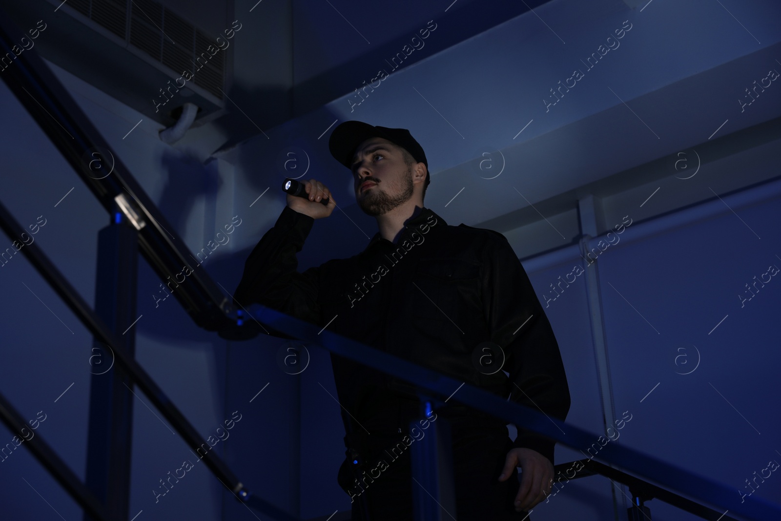 Photo of Male security guard with flashlight on stairs in darkness