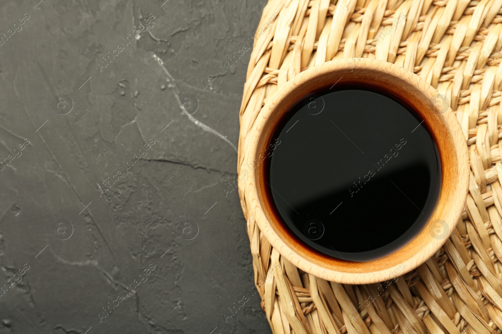 Photo of Soy sauce in bowl on black textured table, top view. Space for text