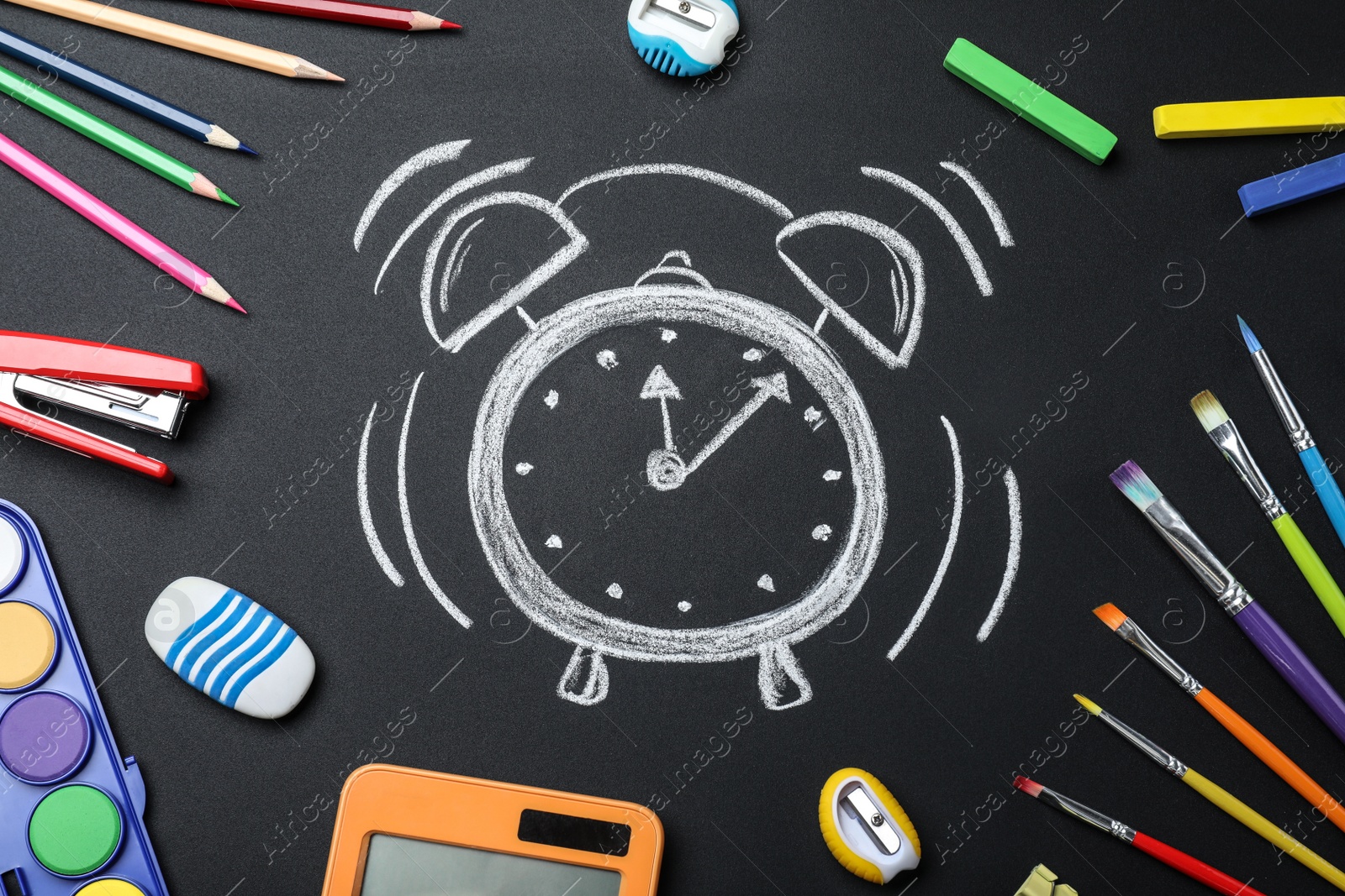 Photo of Flat lay composition with different stationery and drawn alarm clock on blackboard. School time