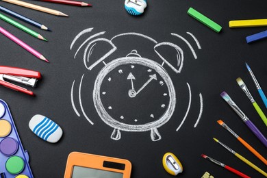 Flat lay composition with different stationery and drawn alarm clock on blackboard. School time